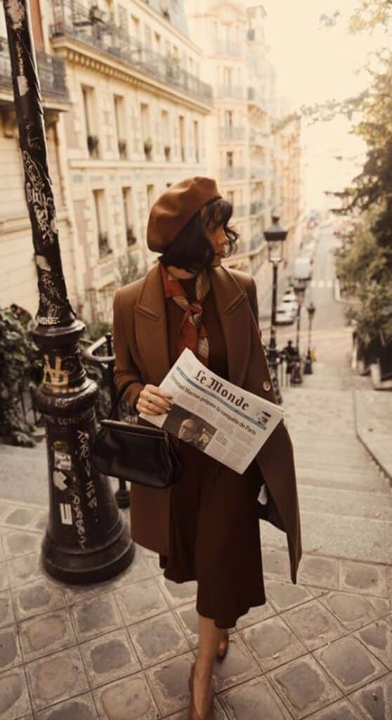 10 outfits elegantes con abrigo perfectos para otoño-invierno 2021 - Handy Home Stylish woman in Parisian street with brown coat and beret, holding a newspaper, descending historic stairs. Elegant urban fashion.