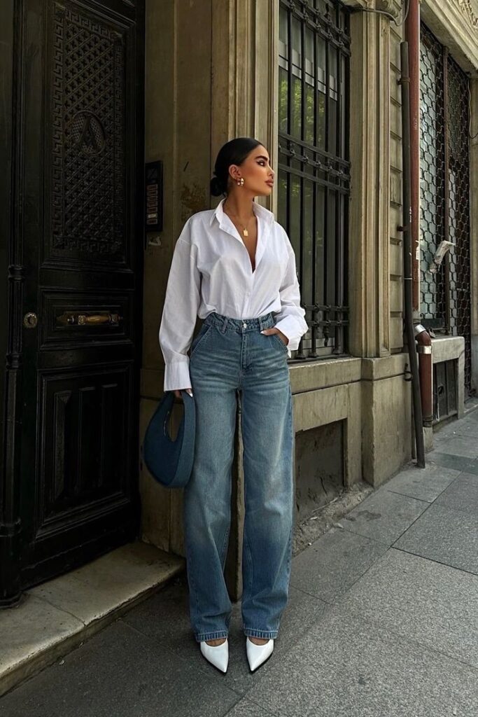 100+ Summer Outfits 2025 PDF _ Capsule Wardrobe Guide _ Vacation City Festival Looks Planner - Handy Home Stylish woman in white shirt and jeans, standing by ornate door, exuding chic urban fashion with elegant accessories.