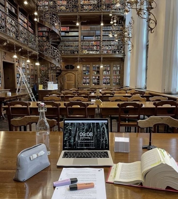 1b10409a-3237-4f3c-b4f8-741e01274621 - Handy Home Elegant library study area with laptop, open book, and stationery on a wooden table, surrounded by towering bookshelves.