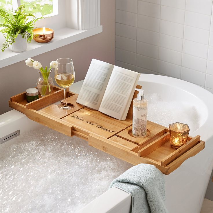 2-in-1 Convertible Bath Caddy _ Personal Creations - Handy Home Bamboo bath tray over a bubble bath with wine, flowers, candle, book, and bath products for a luxurious relaxation experience.
