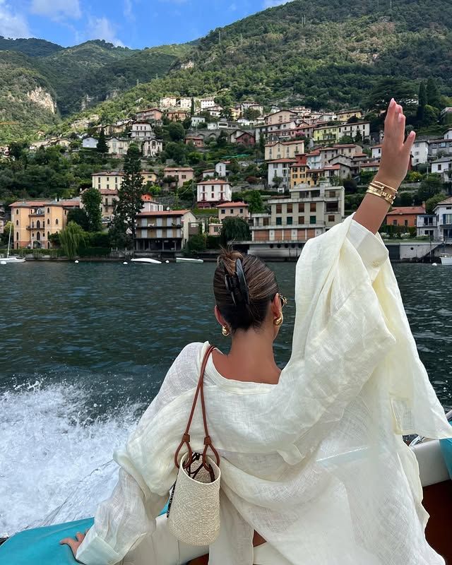 20019836-4cdc-40fb-aee0-ad87bb7fb867 - Handy Home Woman on boat waving at scenic Italian lakeside village with colorful houses and lush hillside.