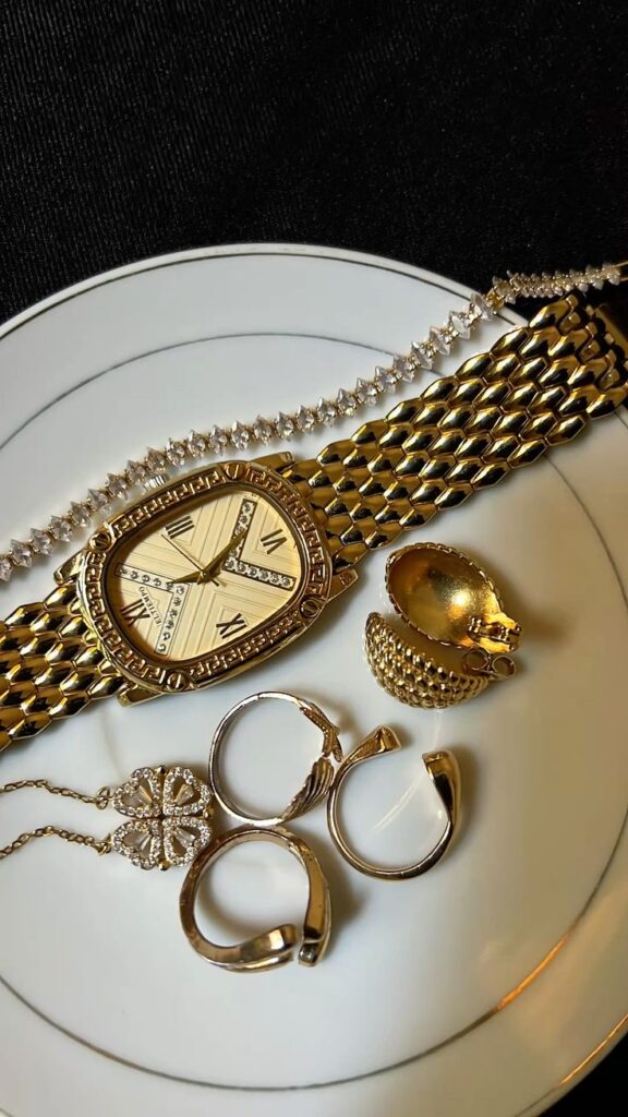 201254ad-440f-4481-940e-0cd2014629d2 - Handy Home Elegant gold watch and jewelry set with rings and necklace displayed on a plate, perfect for classy fashion styling.