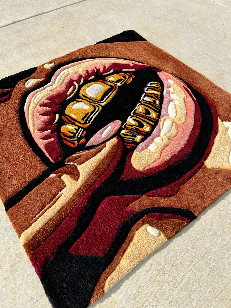 Modern art rug with vibrant colors depicting stylized open mouth with gold teeth, displayed on a concrete surface.