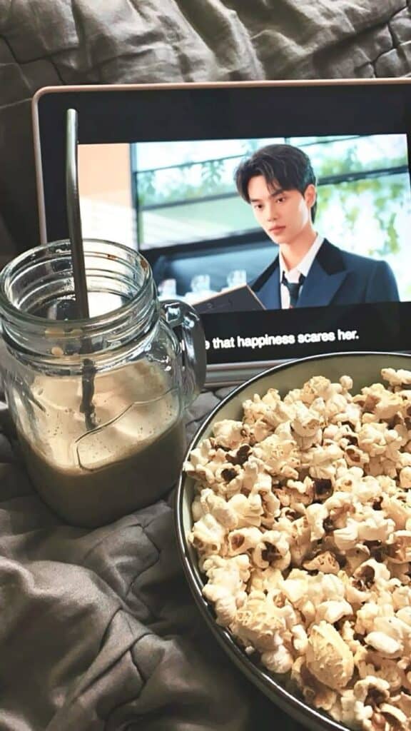 27889d62-e5b1-403e-b37d-b365981cb295 - Handy Home Cozy movie night setup with popcorn and iced coffee in mason jar, watching a show on a tablet with subtitles.