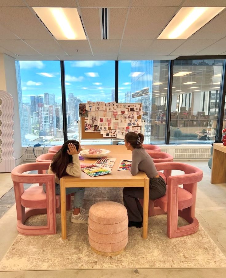 27a25149-3860-4294-9d00-e10dcff55b81 - Handy Home Two people collaborate at a design table with mood boards and color swatches in a modern office with city skyline views.