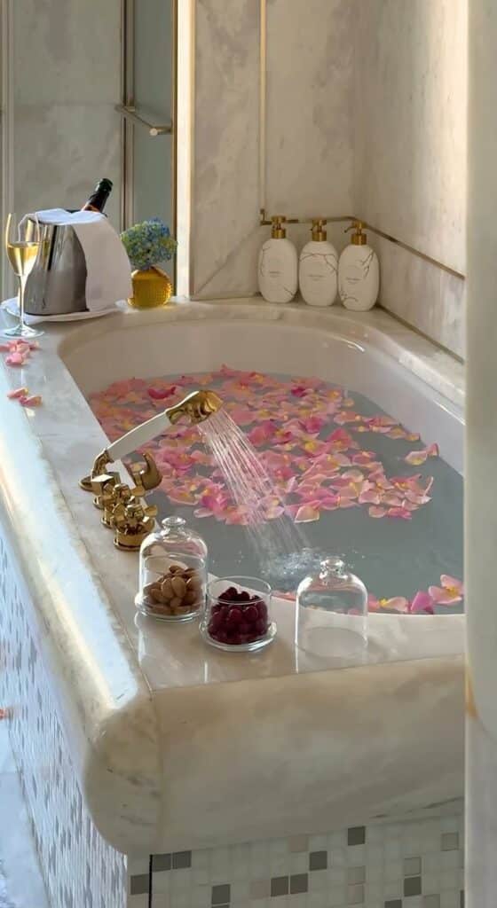 2865ef1a-4b3a-4562-8754-e2e1e0c2e7e5 - Handy Home Luxurious marble bathtub with pink rose petals, champagne, and snacks creates a perfect relaxing spa experience at home.