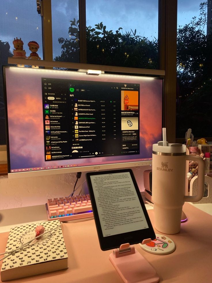 28a0620c-bf0f-4b1d-8d6d-099ac8cbbbcd - Handy Home Cozy workspace setup with a monitor displaying music, a tablet for reading, and a large tumbler, against an evening backdrop.