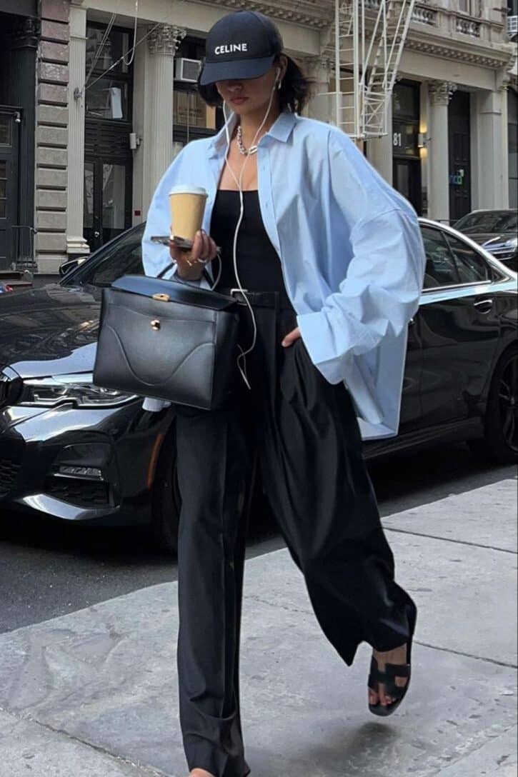 292d21b7-99e7-4844-a74d-c12ec375cde1 - Handy Home Fashionable woman in oversized shirt, cap, and sandals walking in city with coffee and luxury bag. Urban street style fashion.