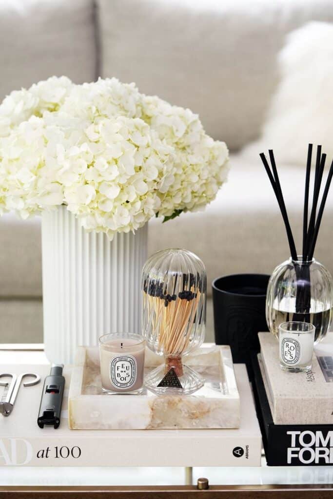 433a6818-75df-4ddc-89b5-7fe61e0ff7b2 - Handy Home Elegant coffee table with white hydrangeas, candles, books, and a diffuser, creating a cozy, sophisticated living room ambiance.