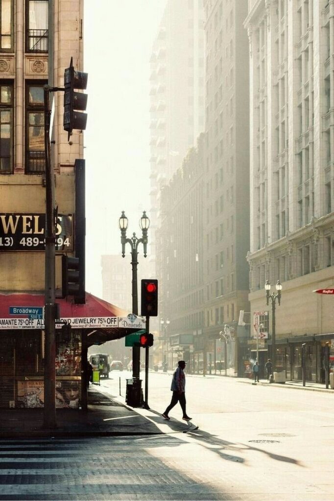 482f2536-ffca-4695-8f1c-9519dc048650 - Handy Home Urban street scene with a person crossing at a traffic light, surrounded by historic buildings under morning sunlight. Street Photography