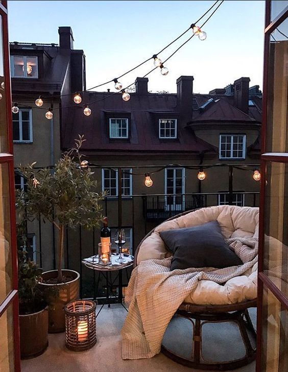 49d2c9d9-1a2c-4fde-9778-0937a8bfe86b - Handy Home Cozy balcony setup at sunset: chair, blanket, pillows, string lights, candle glowing, city view, perfect for relaxing evenings.