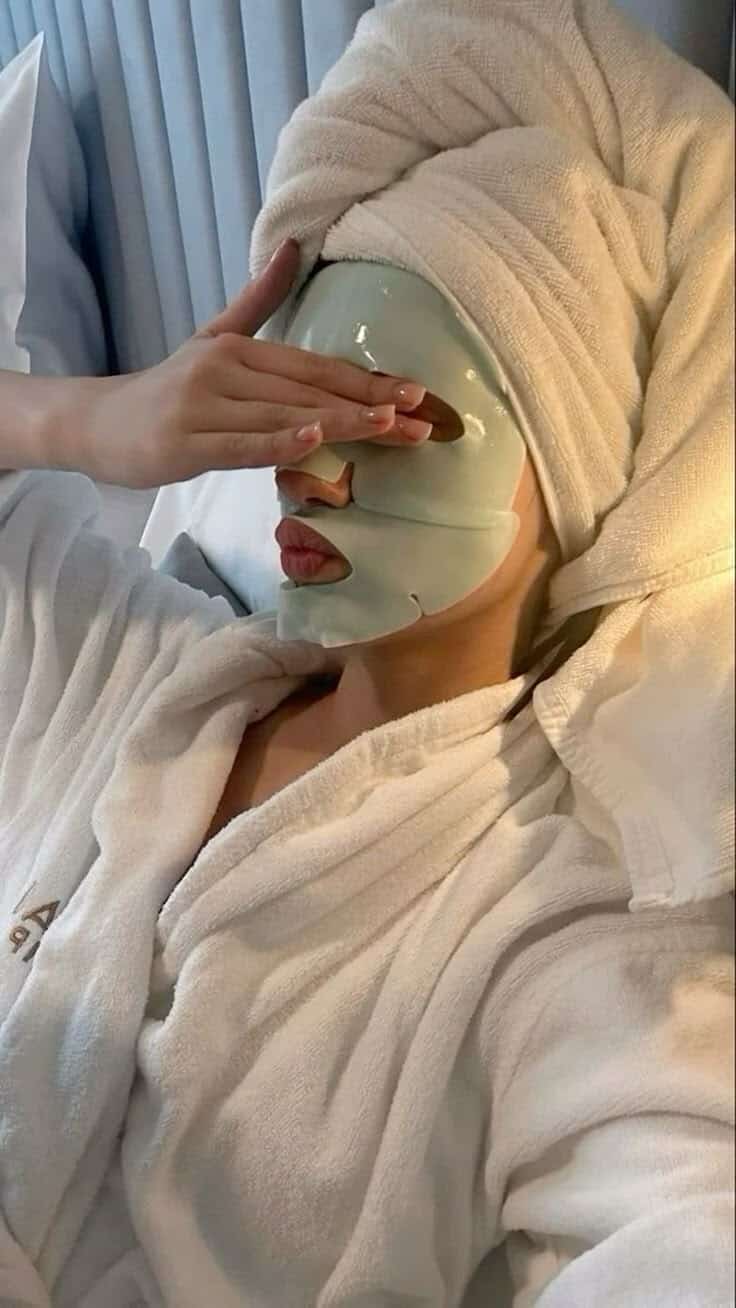 5b59a098-7380-4bb3-ba54-1c2fdf7c9a3e - Handy Home Woman relaxing with a green face mask and towel on head, wearing a bathrobe in a serene setting. Perfect for skincare relaxation.