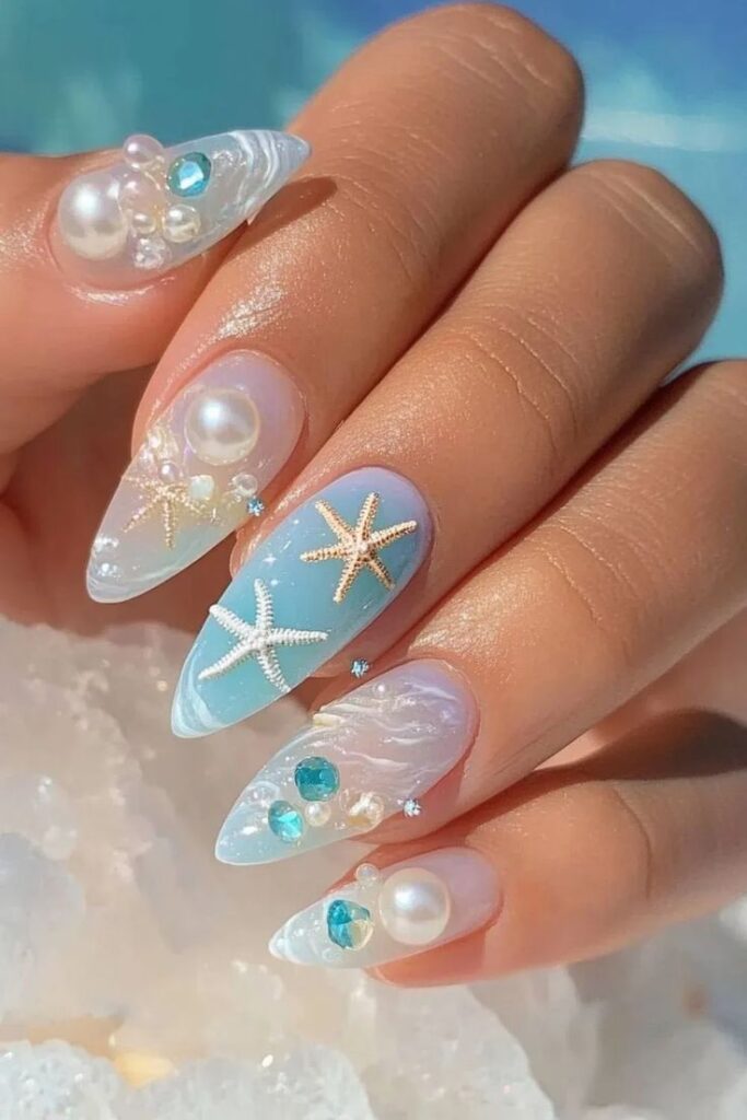63 Sea-Inspired Nails for a Fresh Coastal Vibe - Handy Home Elegant ocean-themed nail art with pearls, sea stars, and blue accents on a hand, evoking a beachy, summer vibe.