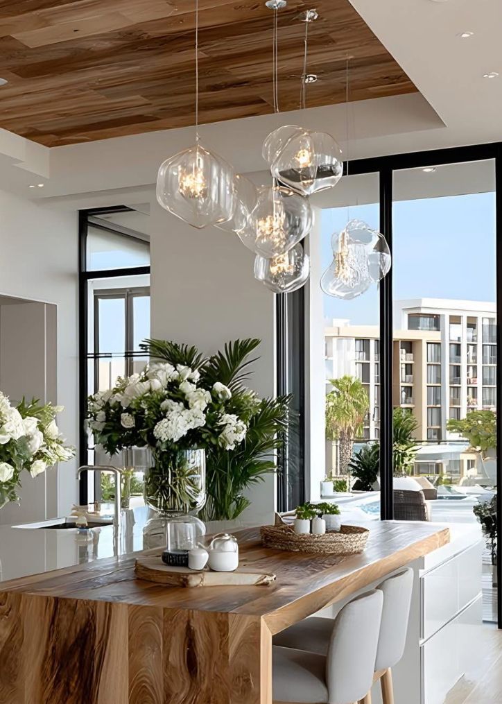 653b4847-f762-41fb-9174-a61d665064f8 - Handy Home Modern kitchen with wooden accents, glass pendant lights, and lush plants by large windows, offering a bright, elegant space.