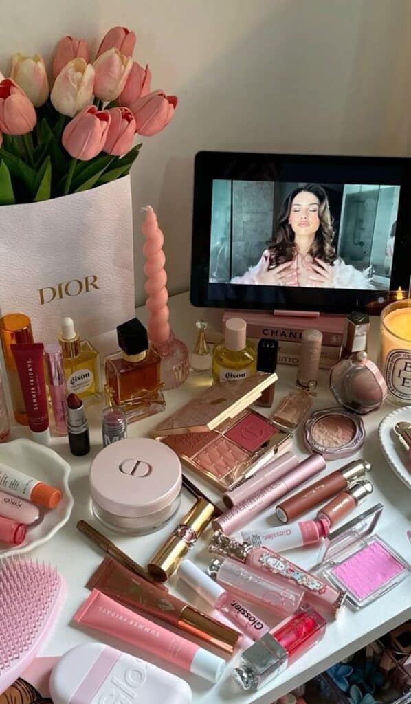 70a68529-8105-4de7-a2c7-053b0312c1e8 - Handy Home Vanity table with makeup, beauty products, pink tulips, and a tablet displaying a beauty tutorial.