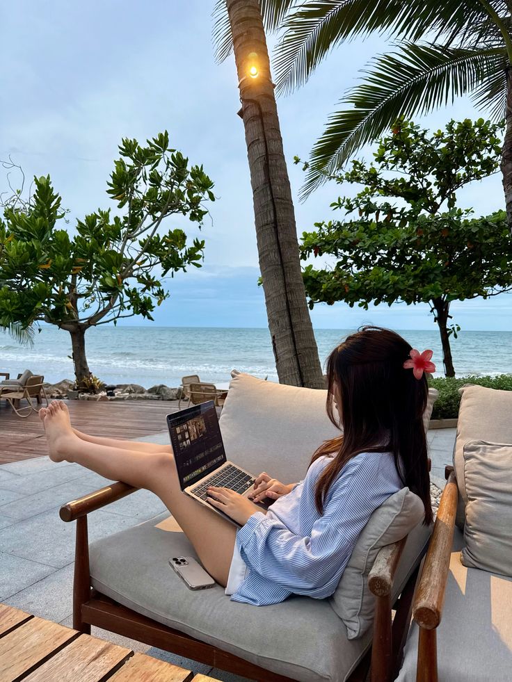 7a812095-afb4-4821-b9c0-b4c796f04422 - Handy Home Person working on a laptop by the ocean under palm trees, enjoying a tropical beach view.