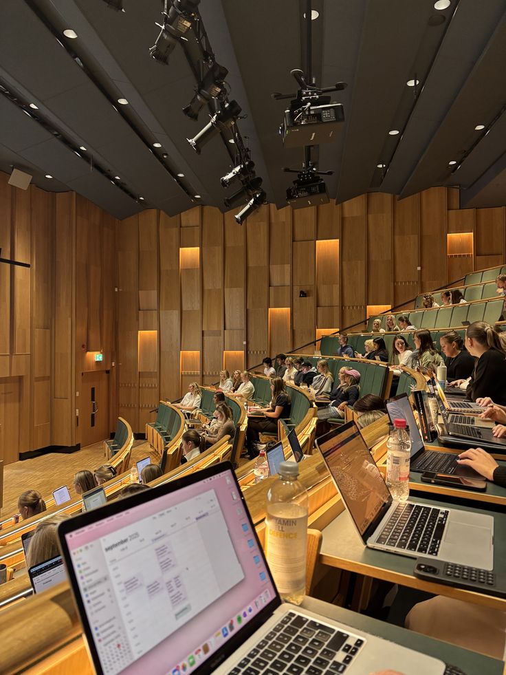802a4095-d618-4d71-93f7-84c89b99bd2c - Handy Home Modern lecture hall with students using laptops in tiered seating, surrounded by warm wood paneling and attentive attendees. Time Management Hacks