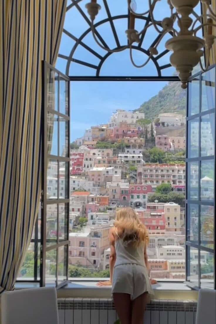 81757d8a-aa4d-454a-81e9-04812fdc1d58 - Handy Home Woman gazing out a window at colorful Positano houses, Italy. Scenic view enhances the cozy interior ambiance.
