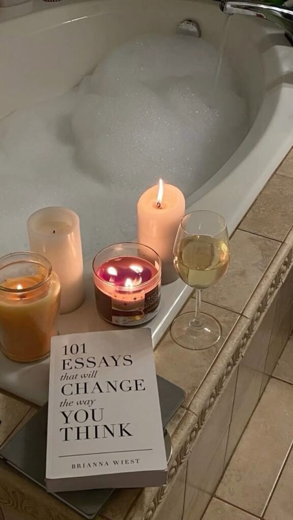 839c967f-4d3e-43e3-9032-c565d7a40ee7 - Handy Home Cozy bubble bath with candles, a book titled 101 Essays, and a glass of wine; perfect relaxation setup.