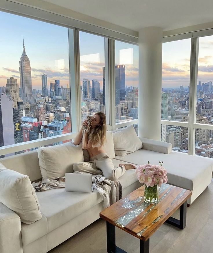 840ccbb2-a3ca-4bc2-81d0-617863716db9 - Handy Home Cozy living room with city view, woman relaxing on sofa with coffee and laptop.