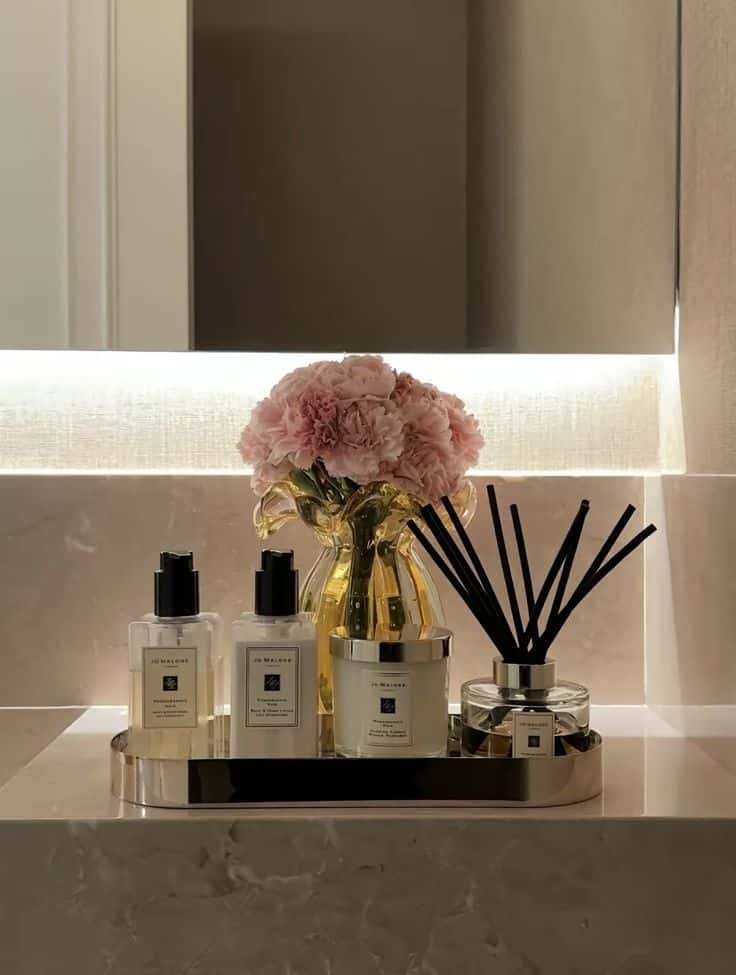 8b6904bf-a72f-4db6-bc46-da81d9230a2d - Handy Home Luxury bathroom decor with scented candles, reed diffusers, and pink flowers in a golden vase, creating an elegant and relaxing ambiance.