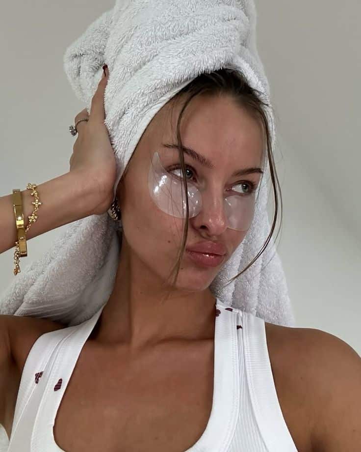 8d5b06f9-5609-4237-bcb3-50f57ceeb3aa - Handy Home Woman with eye patches and towel on head, wearing a white tank top, showing a skincare routine.