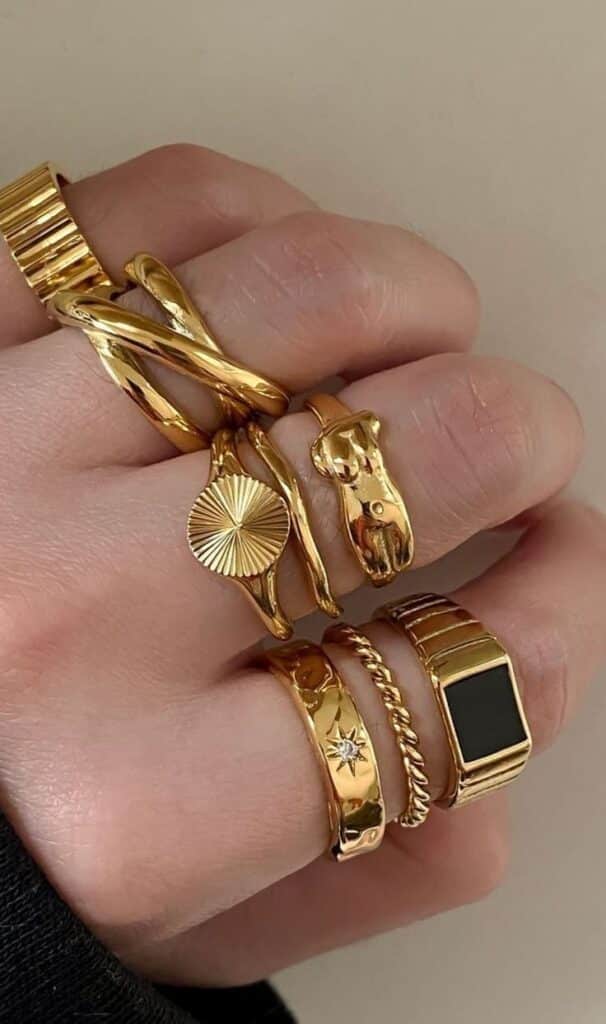 9cd67e8b-11b3-4a41-80be-ddfaead673b6 - Handy Home Close-up of a hand wearing multiple stylish gold rings with unique designs, showcasing modern jewelry fashion.