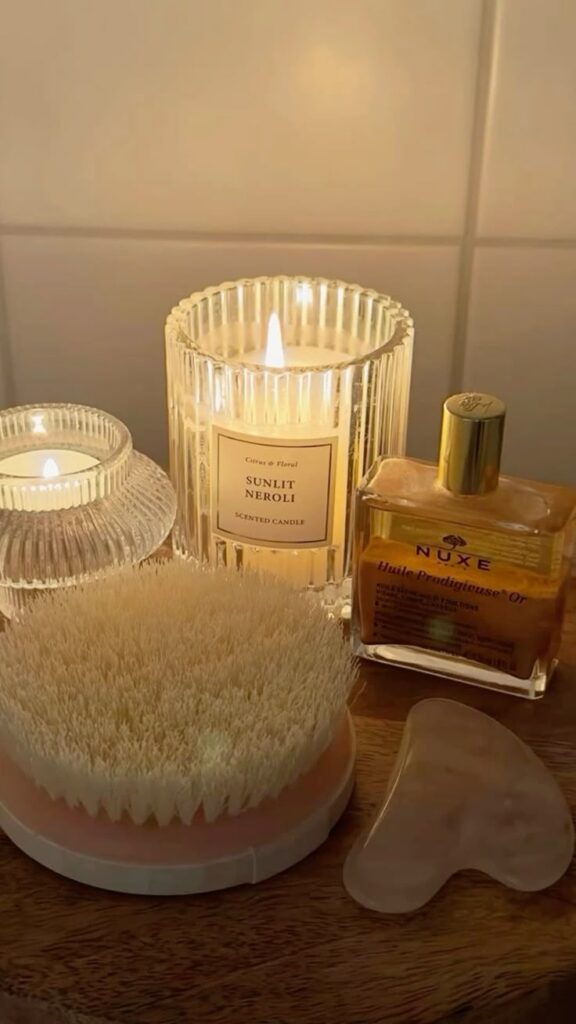 Cozy night✨ - Handy Home Cozy spa setup with lit scented candles, body oil, gua sha, and brush on a wooden surface for relaxing self-care routine.