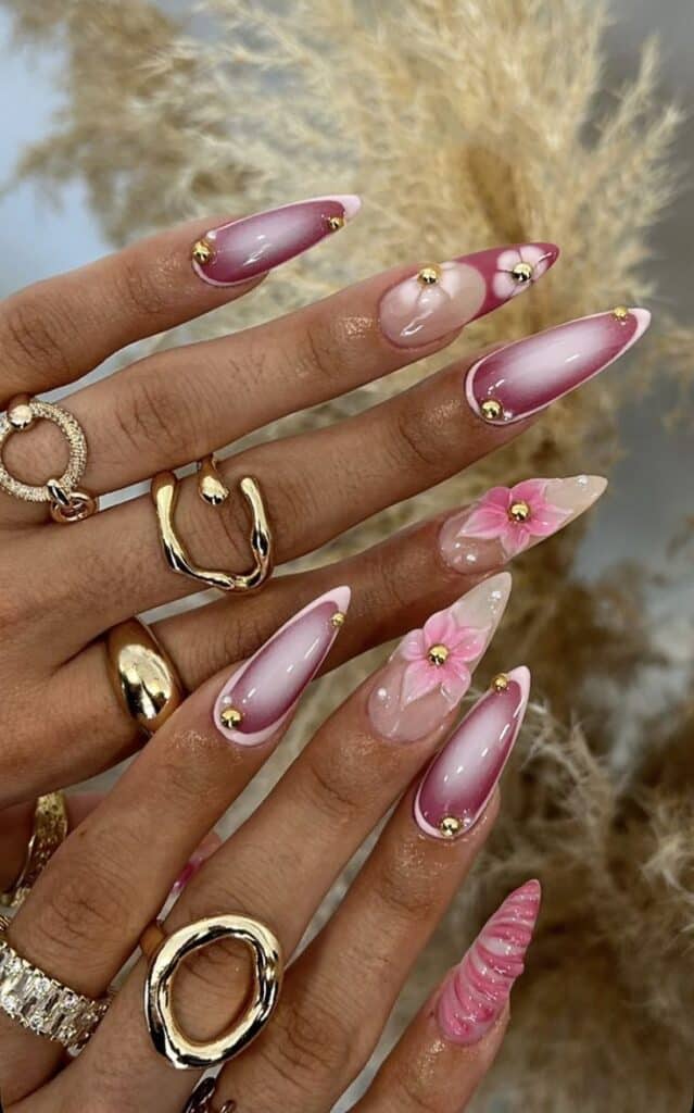 Follow for more 💕 - Handy Home Elegant pink and gold nail art with floral accents, adorned with rings. Perfect for stylish manicure inspiration.