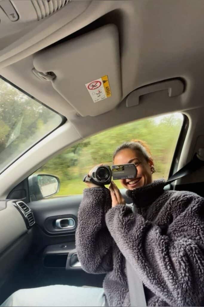 Friends travel - Handy Home Person in a car holding a video camera, capturing moments on a road trip. Cozy sweater, travel vibes.