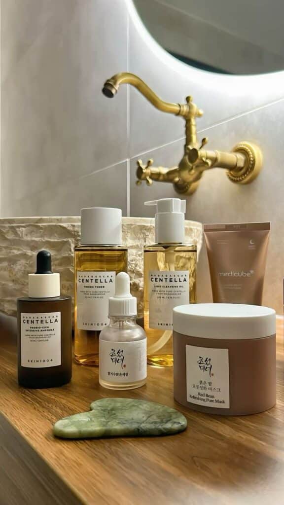 Korean Skincare products 👀💁🏻_♀️💗 - Handy Home Skincare products on bathroom counter, featuring toners, cleansing oil, serums, masks, and a gua sha tool next to a vintage-style faucet.