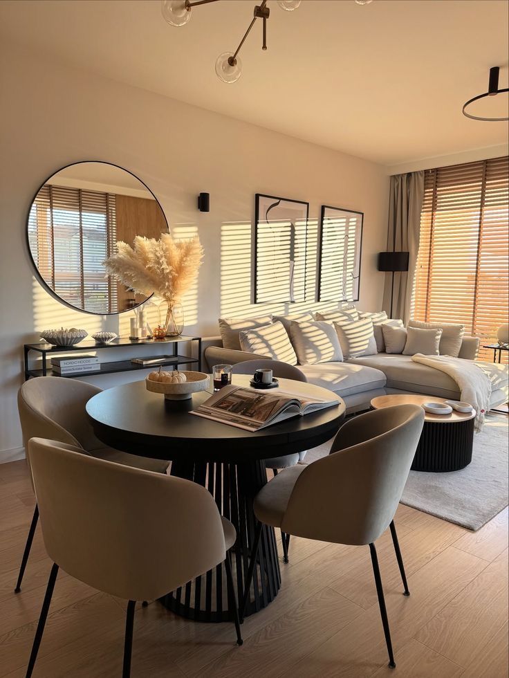 My perfect slow morning starts here_ 🌾 - Handy Home Modern living room with beige accents, round mirror, cozy sofa, dining set, and sunlight filtering through blinds. Elegant and inviting decor.