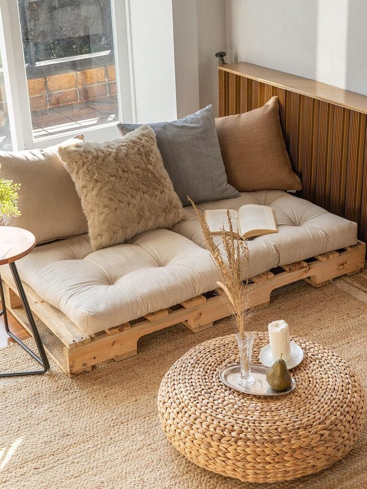 Natural Beige Linen Cushion - Handy Home Cozy living room with pallet sofa and cushions, wicker table, open book, candle, and decorative pear, bathed in natural light.