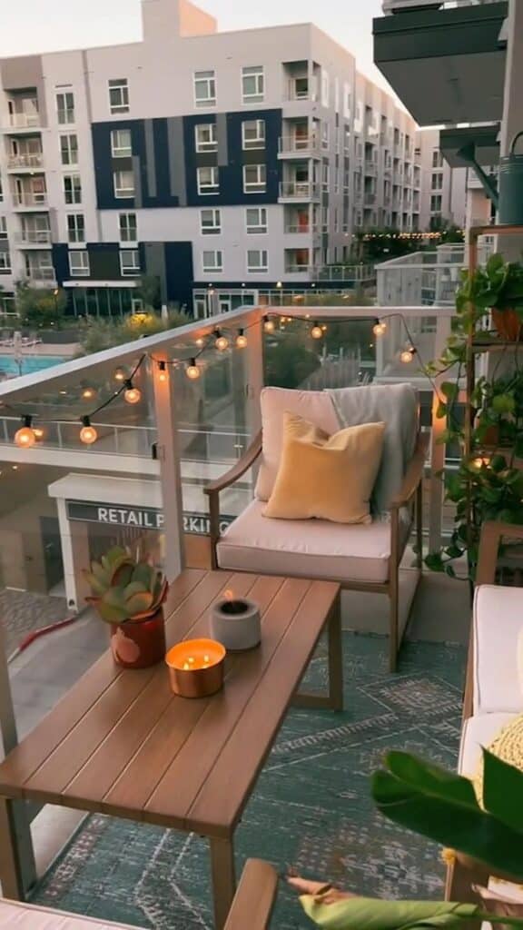 Outdoor Area Prep - Handy Home Cozy apartment balcony with seating, plants, and string lights, overlooking modern urban buildings. Ideal for relaxation.