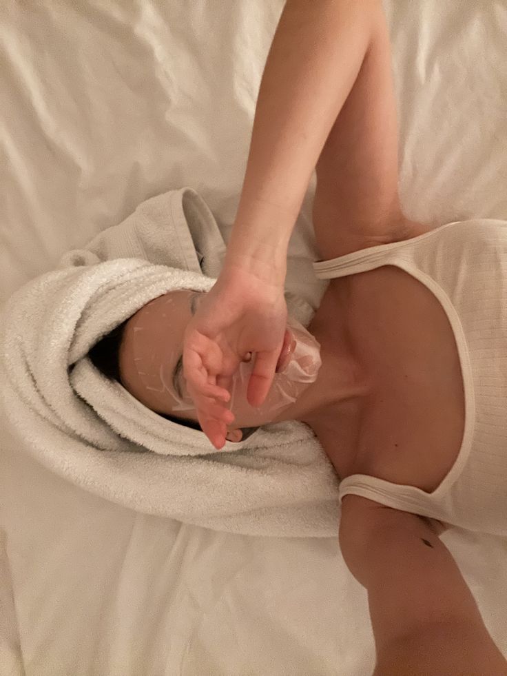 Self care sundayzzz - Handy Home Person relaxing with a towel and face mask, lying on a bed. Spa day, self-care routine, white tank top.
