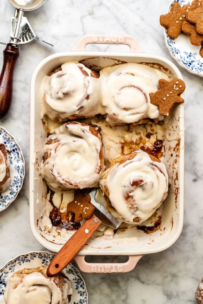 Small Batch GIANT Gingerbread Cinnamon Rolls - Handy Home Creamy frosted cinnamon rolls in a baking dish with gingerbread cookie toppers, perfect for a festive treat.