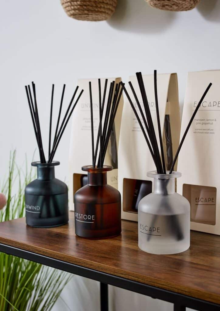 Spa Reed Diffuser - Handy Home Three aromatic reed diffusers labeled Unwind, Restore, Escape, on a wooden table, with packaging in the background.