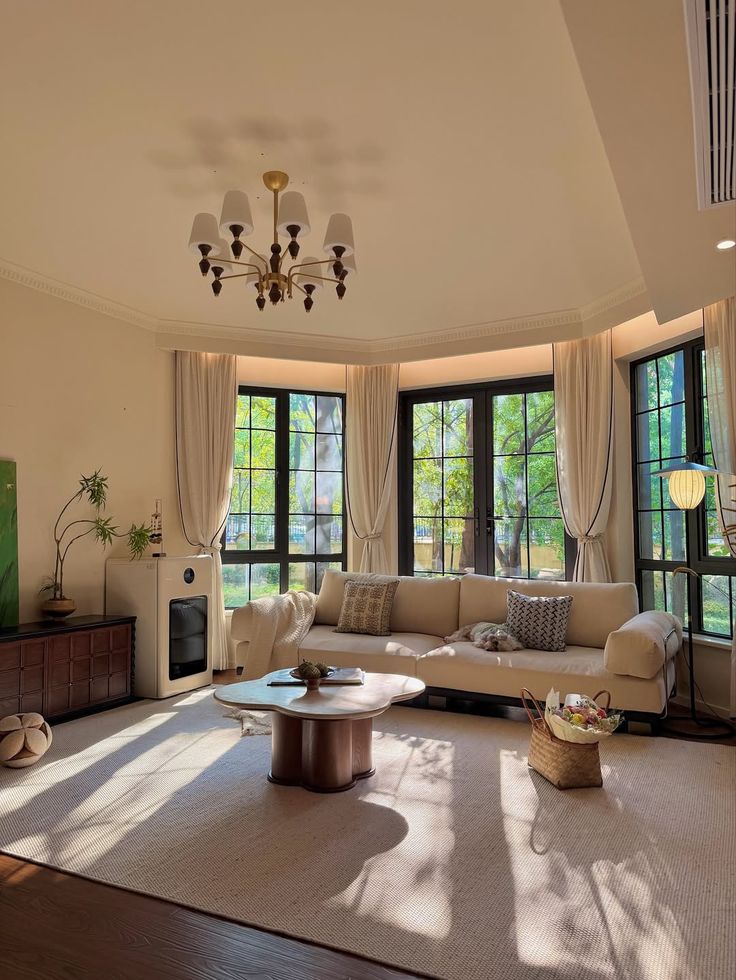 _Sunlight Serenity in a Cozy Living Room__ - Handy Home Bright living room with cozy sofa, large windows, elegant chandelier, wooden table, and soft lighting.