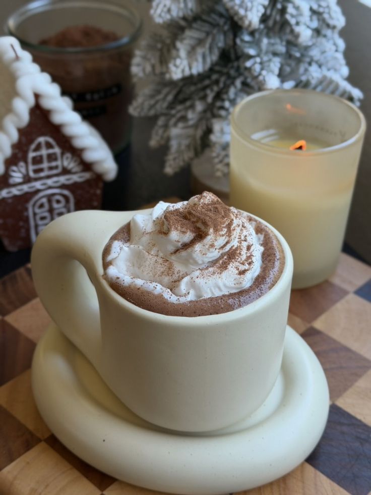 The Coziest Homemade Hot Chocolate Powder Made in 5 Minutes - What Robin Eats - Handy Home Cozy winter scene: Hot chocolate with whipped cream in a mug, surrounded by a candle, gingerbread house, and frosted tree.