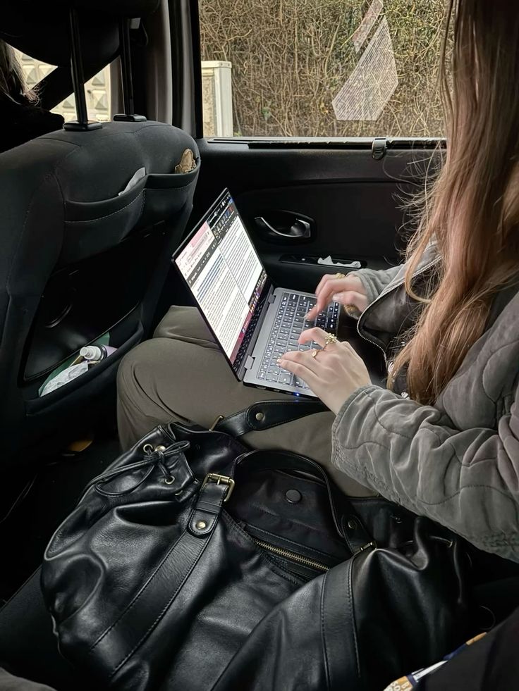Work girl - Handy Home Woman working on a laptop in a car, typing with a black bag nearby. Efficient mobile office setup during travel.