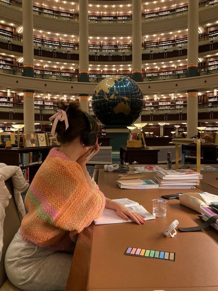 a0d78273-8654-47fe-9dda-420082111b98 - Handy Home Person studying in a grand library with a globe, wearing headphones and surrounded by books and pastel highlighters.