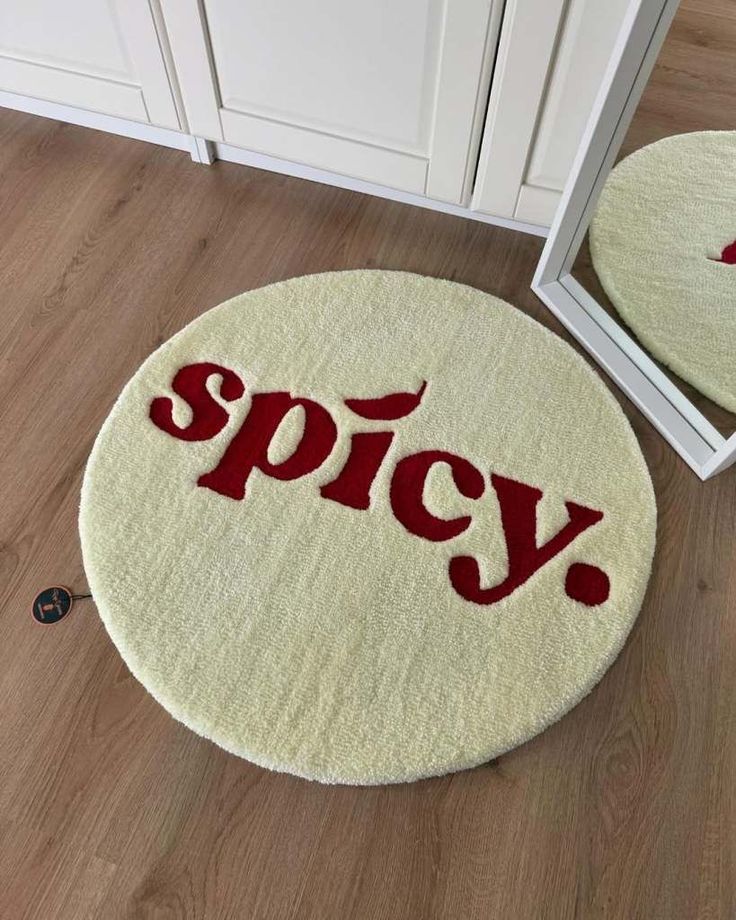 Round white rug with the word spicy in bold red letters on wood floor, reflected in a mirror.