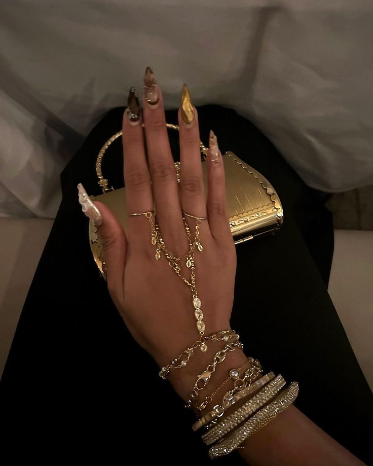 aenjewels - Handy Home Elegant hand jewelry featuring gold rings, bracelets, and a decorative chain with a gold clutch and manicure in the background.