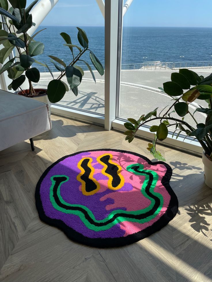 A vibrant abstract rug with colorful designs in a bright room overlooking the ocean, surrounded by potted plants.