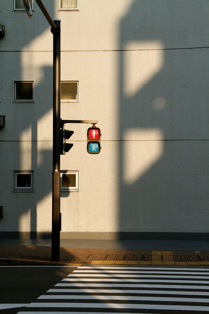 e2caa60e-a5cc-4ab4-beca-7e090307901f - Handy Home Traffic light at a pedestrian crossing on a sunny day, casting shadows on a building with small windows in the background.