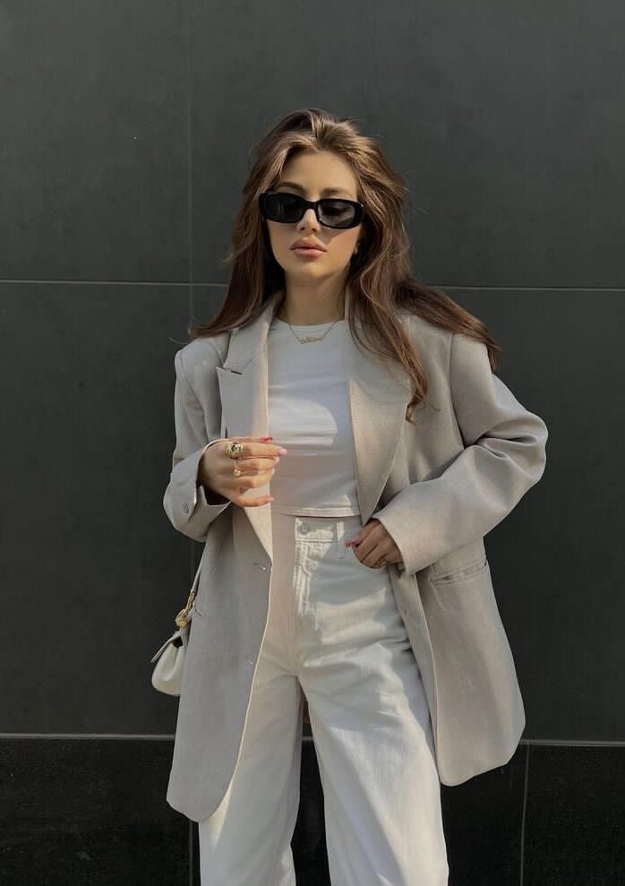 ed34c84e-ea12-447f-8aa1-4f7f55f67a44 - Handy Home Stylish woman in sunglasses wearing a beige blazer and white pants, posing confidently against a dark background. Fashionable look.