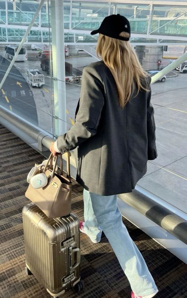 efda967b-3b05-4a98-a37c-f6b6b91009e2 - Handy Home Traveler with suitcase and handbag walks in airport terminal, clad in blazer and jeans.