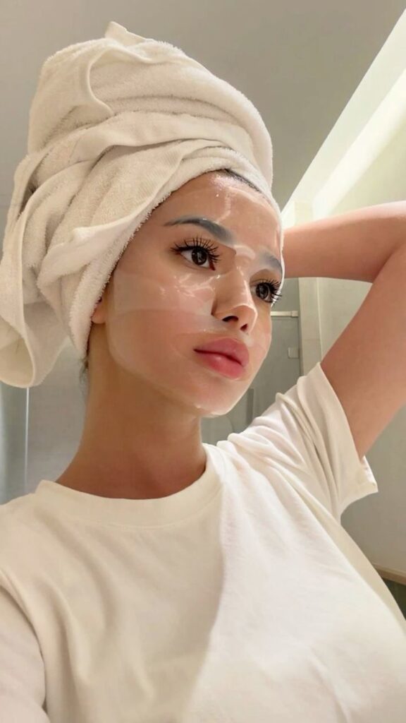 fee36e36-5315-410b-9501-7ce7863f37c7 - Handy Home Person with a towel on head wearing a face mask and white shirt, practicing self-care and skincare routine.