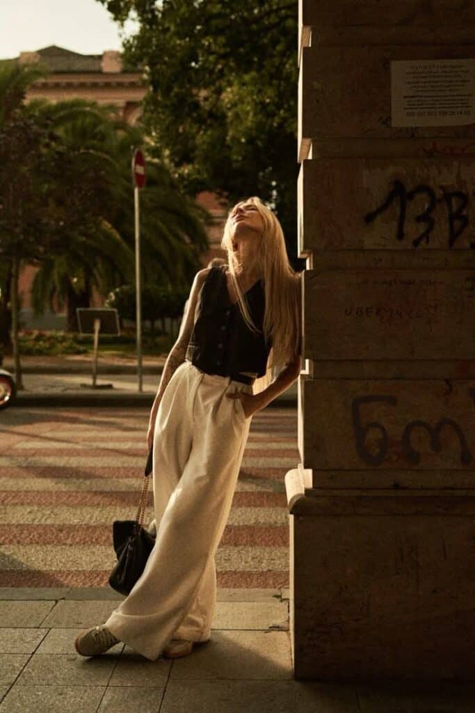 photo - Handy Home Stylish woman in wide-leg pants and vest leans against a sunlit wall, embracing urban fashion with a relaxed, elegant pose.