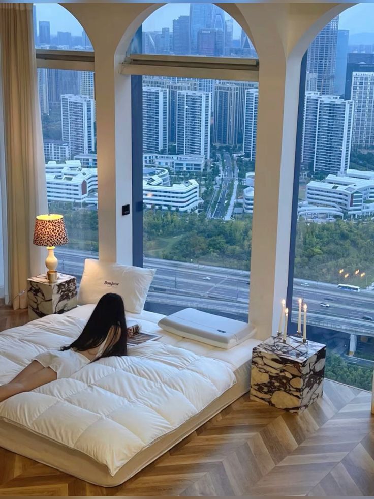 skbily - Handy Home Cozy bedroom with a city view, featuring a woman relaxing on a bed by large windows, capturing a serene urban lifestyle.